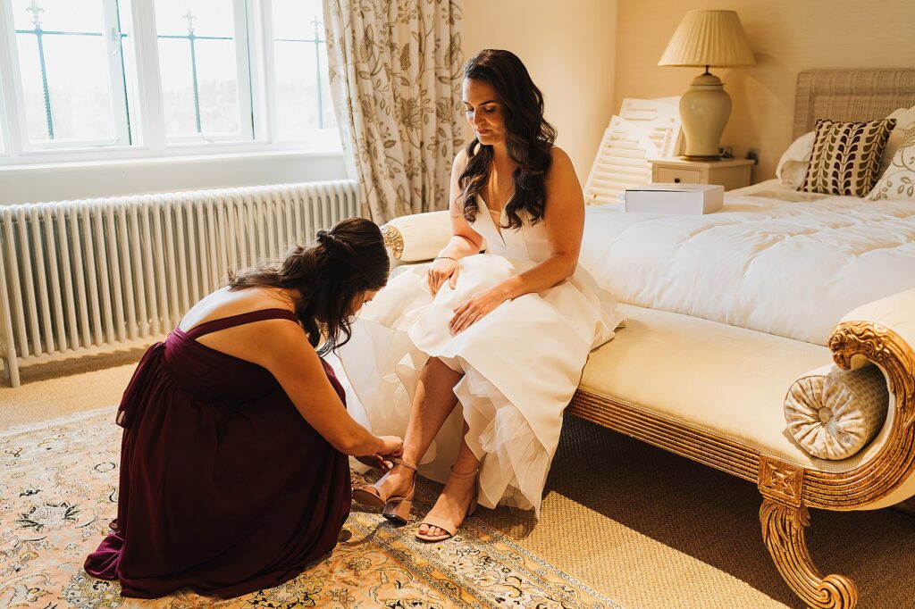 Bride sitting down in the Grange at Hencote as her sister puts on her wedding shoes for her // Shrewsbury wedding photographer