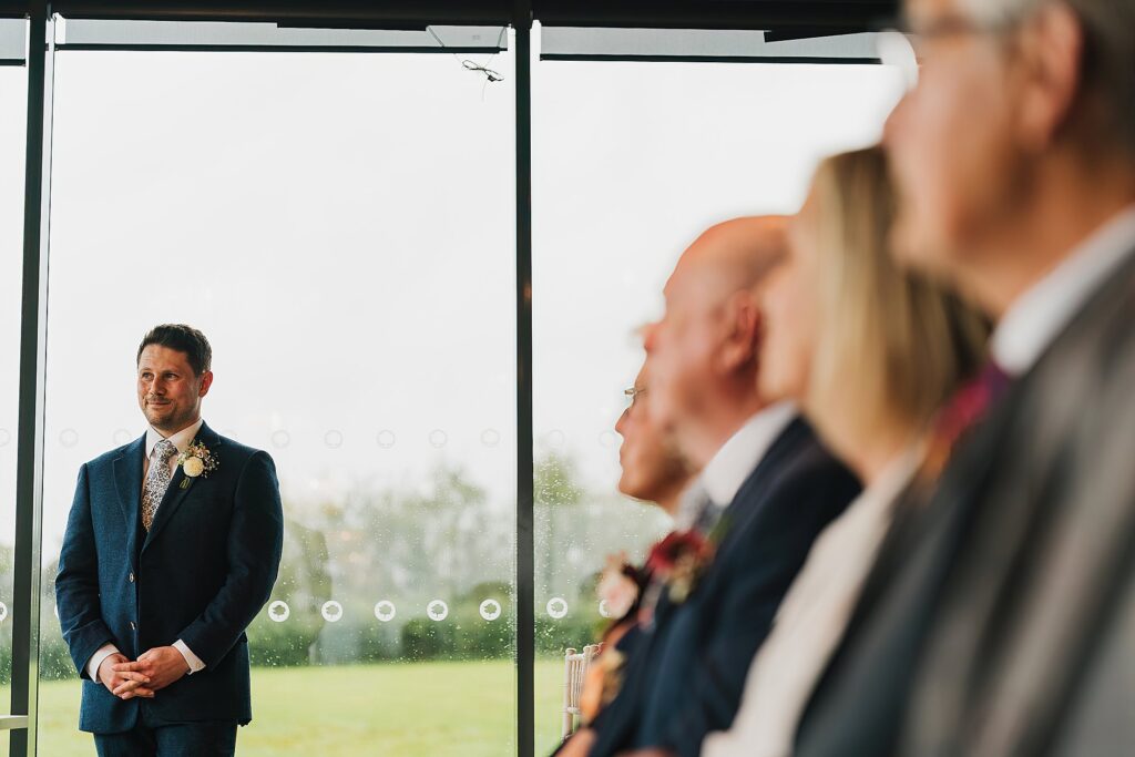 Groom waiting at the top of the aisle at Hencote Estate, looking very excited to see his bride coming down the aisle