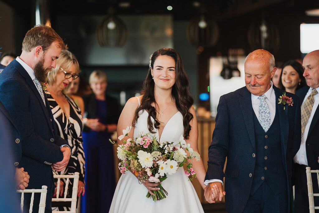 Bride walking down the aisle with the biggest beaming smile and her dad looking down at their hands // Shrewsbury Wedding Photographer