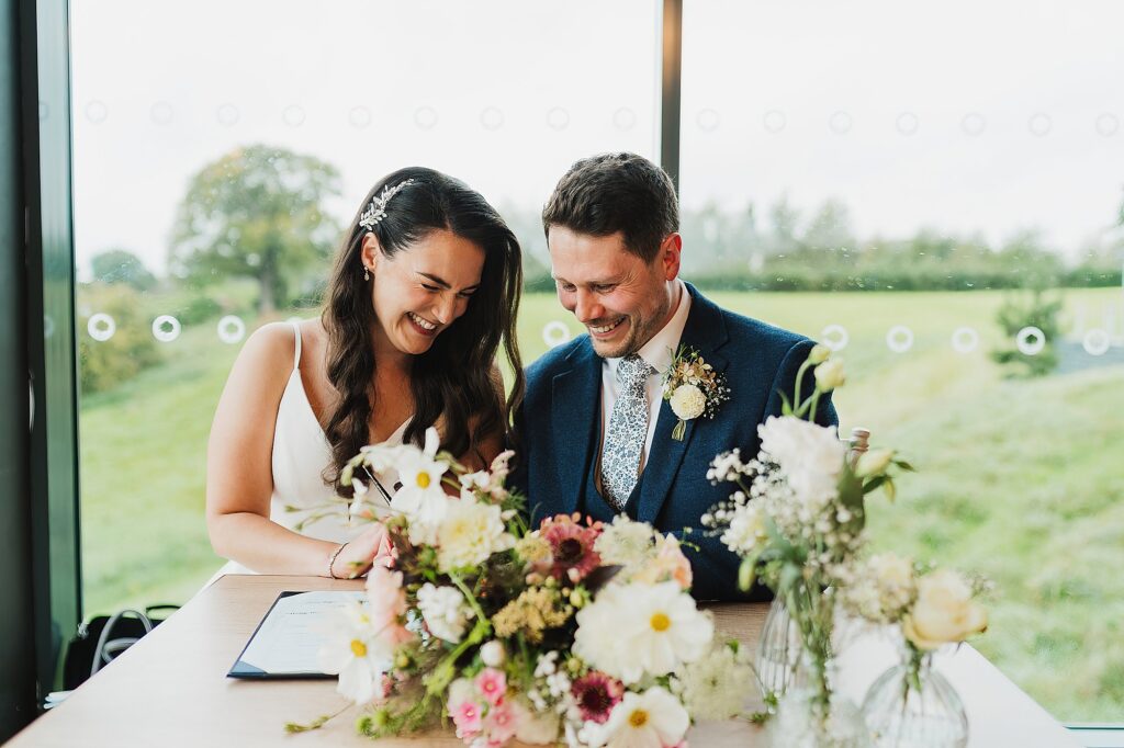 Bride and Groom giggling between themselves as they sign the register at Hencote Estate // Charlotte Giddings Photographer