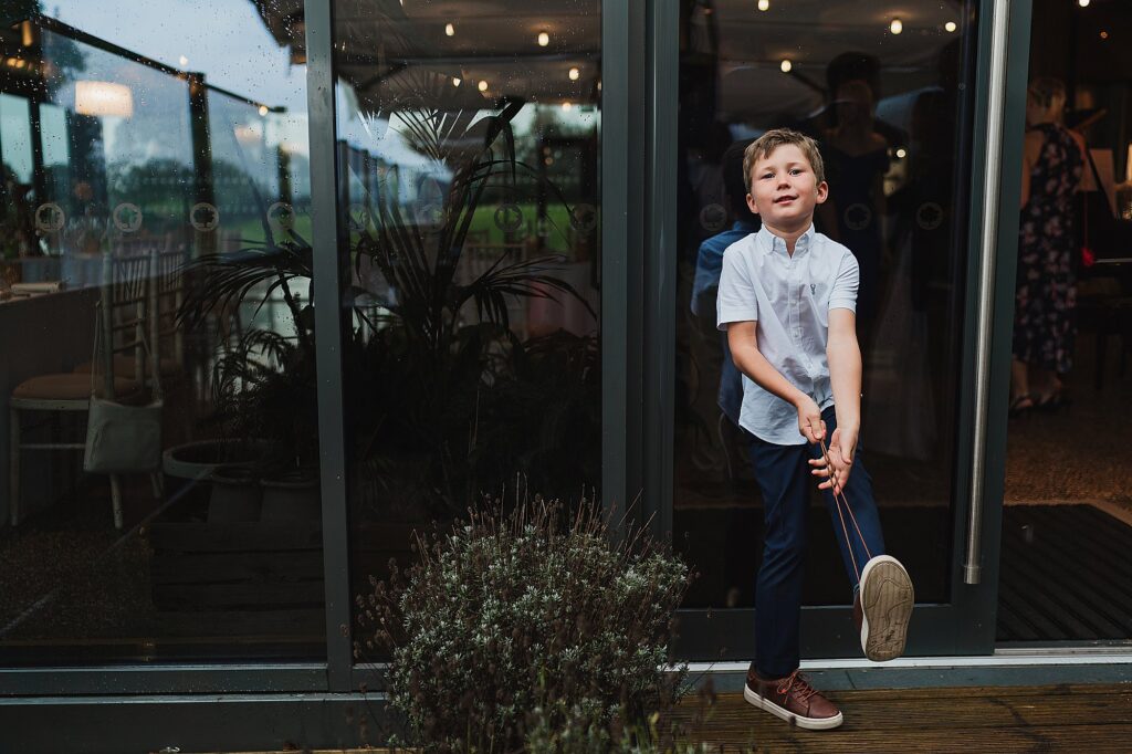Little boy standing against the windows pulling at his shoe laces // Wedding Photographer Shrewsbury
