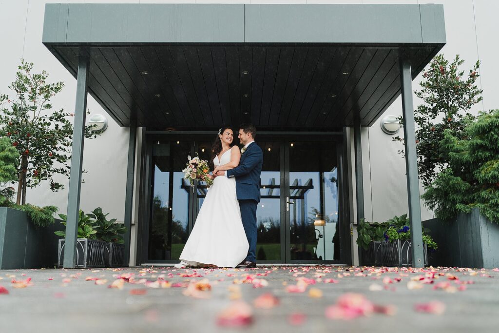 Bride and Groom cuddling outside the Hencote Estate Restaurant after the confetti tunnel and lots of colourful confetti on the pavement
Charlotte Giddings Photography