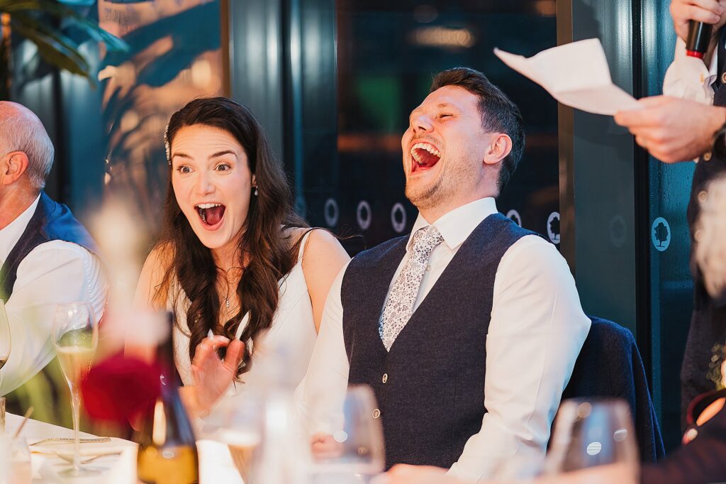 Bride and Groom laughing and equally looking shocked as the best man does his speech // Shropshire Wedding Photography