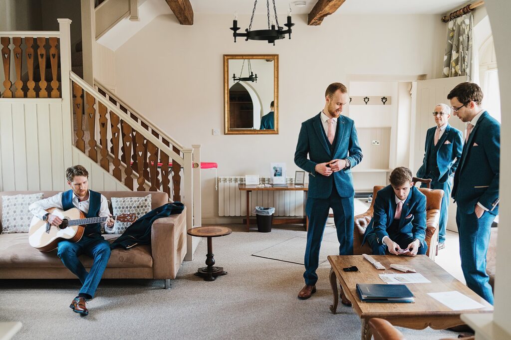 Groom and groomsmen, getting ready in the courtyard cottages, playing the guitar, Combermere Abbey, Shropshire
