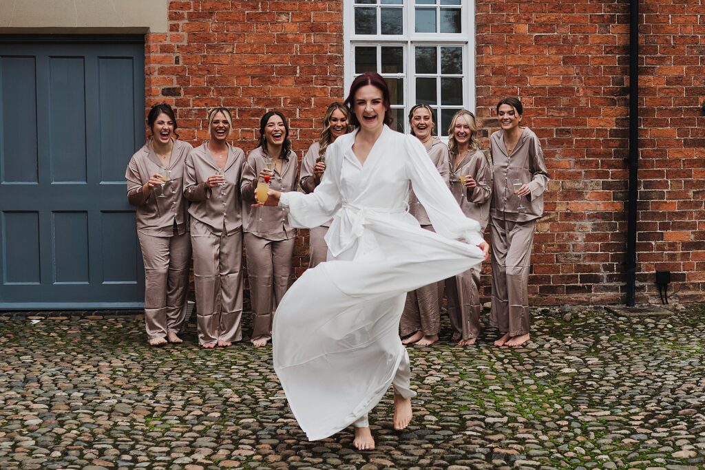 Bride walking in the courtyard at
Combermere Cottages with the bridesmaids giggling in the background, Combermere Abbey, Whitchurch, Shropshire