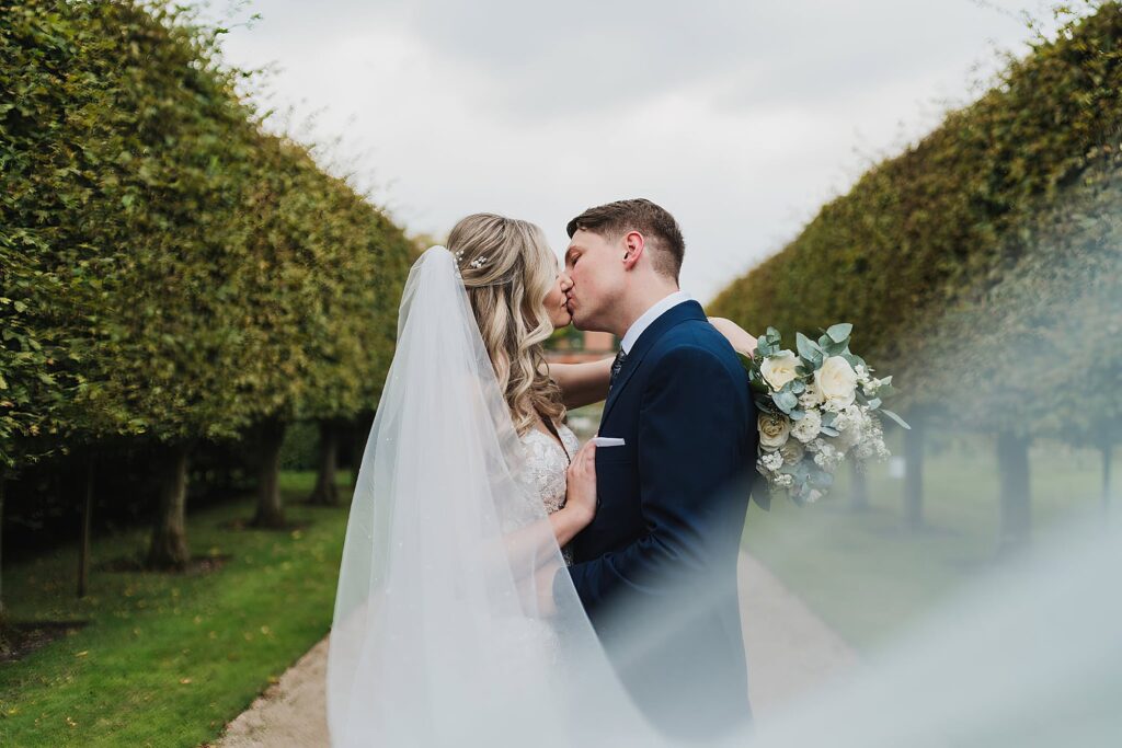 Bride and Groom kissing in the tree lined pathway at Combermere Abbey, Shropshire Wedding Photographer