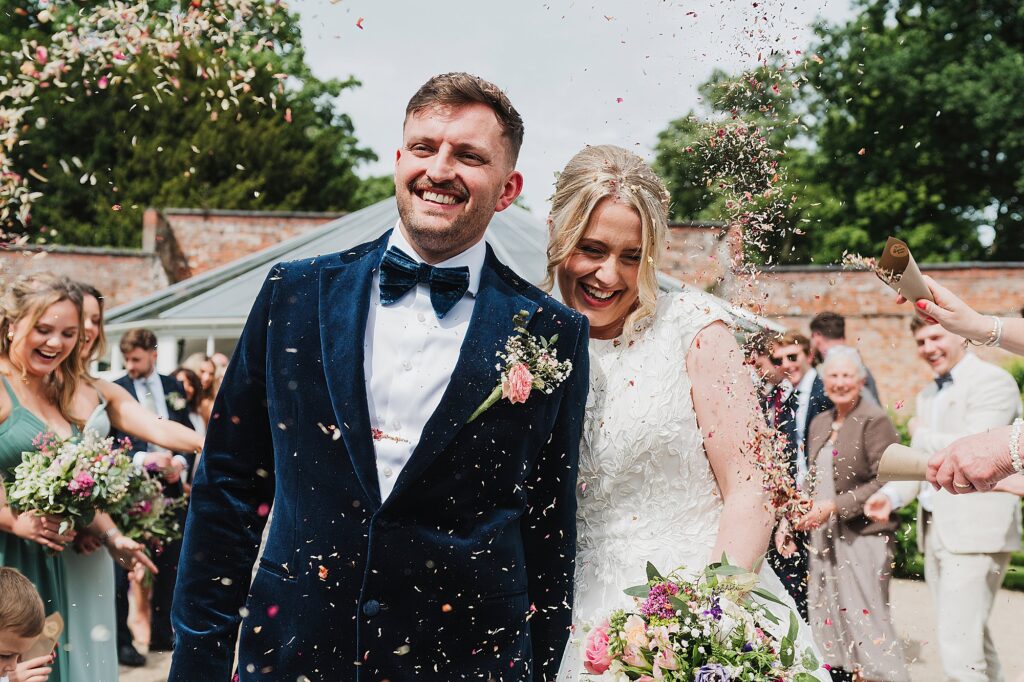 Bride and Groom walking through the confetti tunnel outside Combermere Abbey's Glasshouse