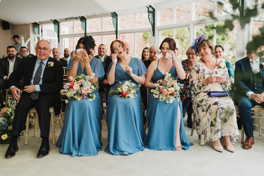 Bridesmaids and bride's parents shedding tears during the ceremony at Combermere Abbey in the Glasshouse