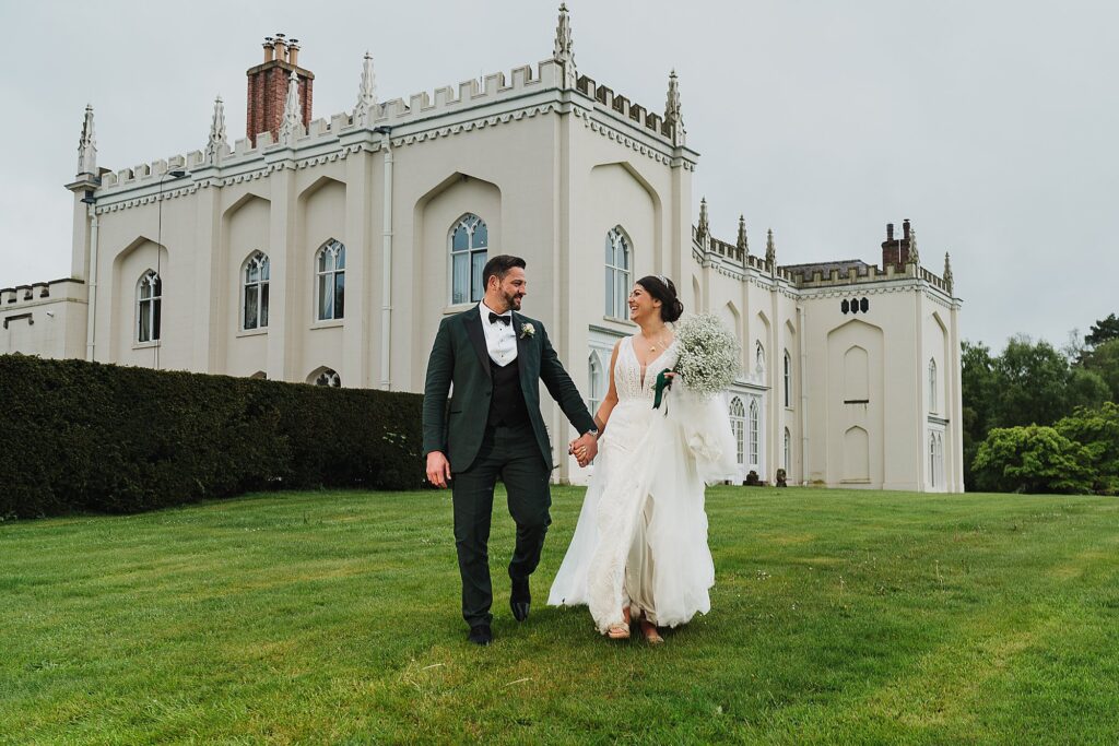 Bride and Groom walking outside of Combermere Abbey building looking lovingly at one another