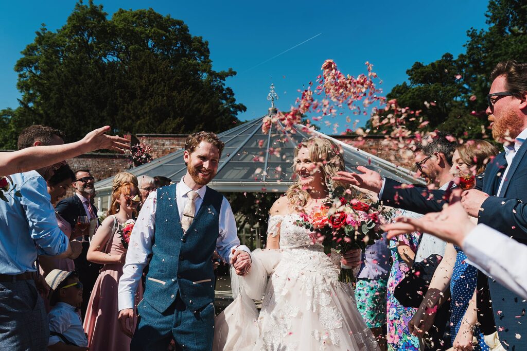 Bride and Groom walking through confetti tunnel with beautiful blue sky outside the Glasshouse, Combermere Abbey