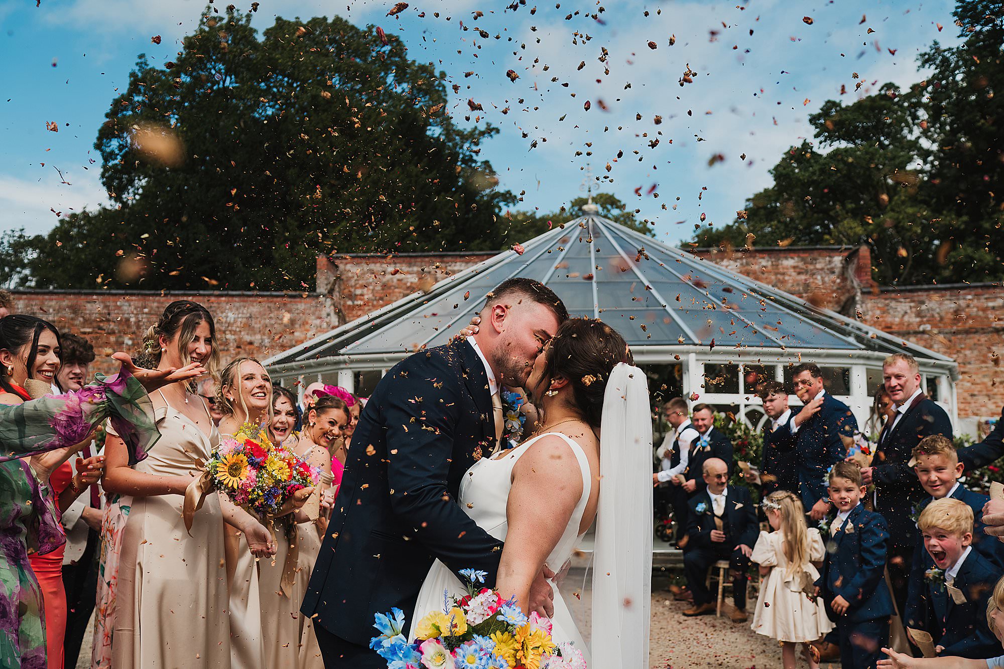 Charlotte Giddings Photography Shropshire Wediding Photographer_1034 Bride and Groom at Combermere Abbey Wedding kissing outside the Glasshouse covered in confetti