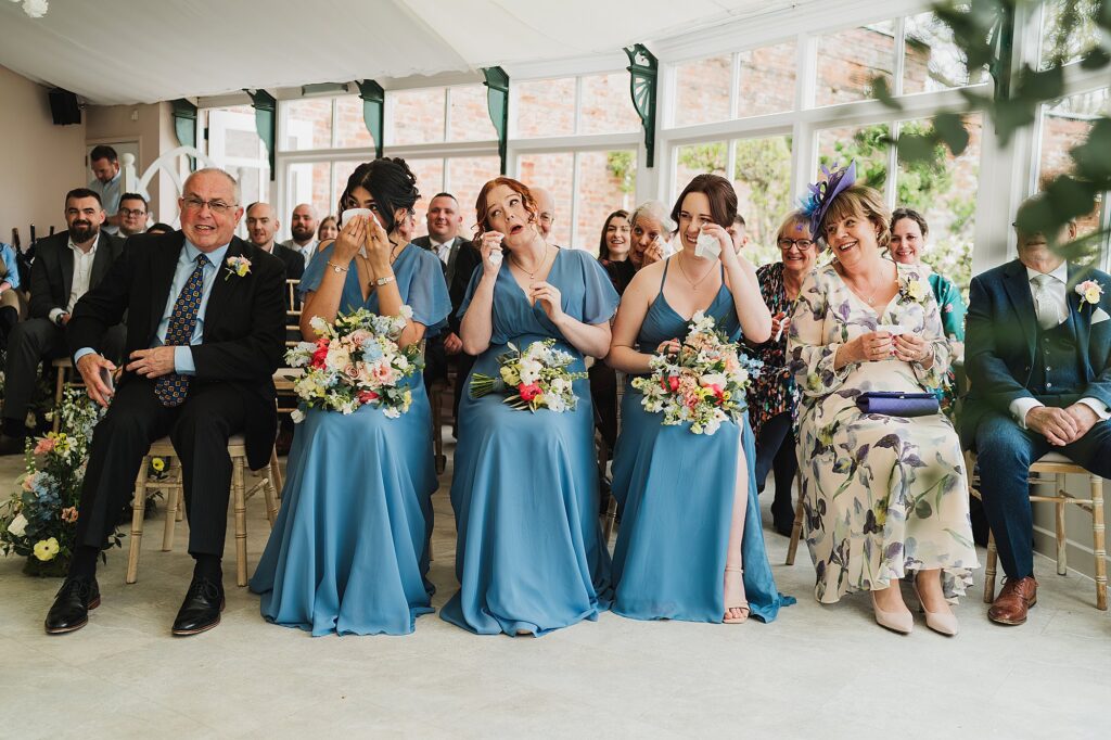 Bridesmaids in the front row all whipping away happy tears at Combermere Abbey in the Glasshouse