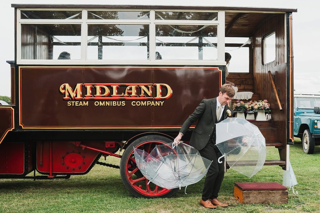 Grooms man trying to get umbrellas ready for the bridemaids, juggling them between his legs // Shropshire Wedding