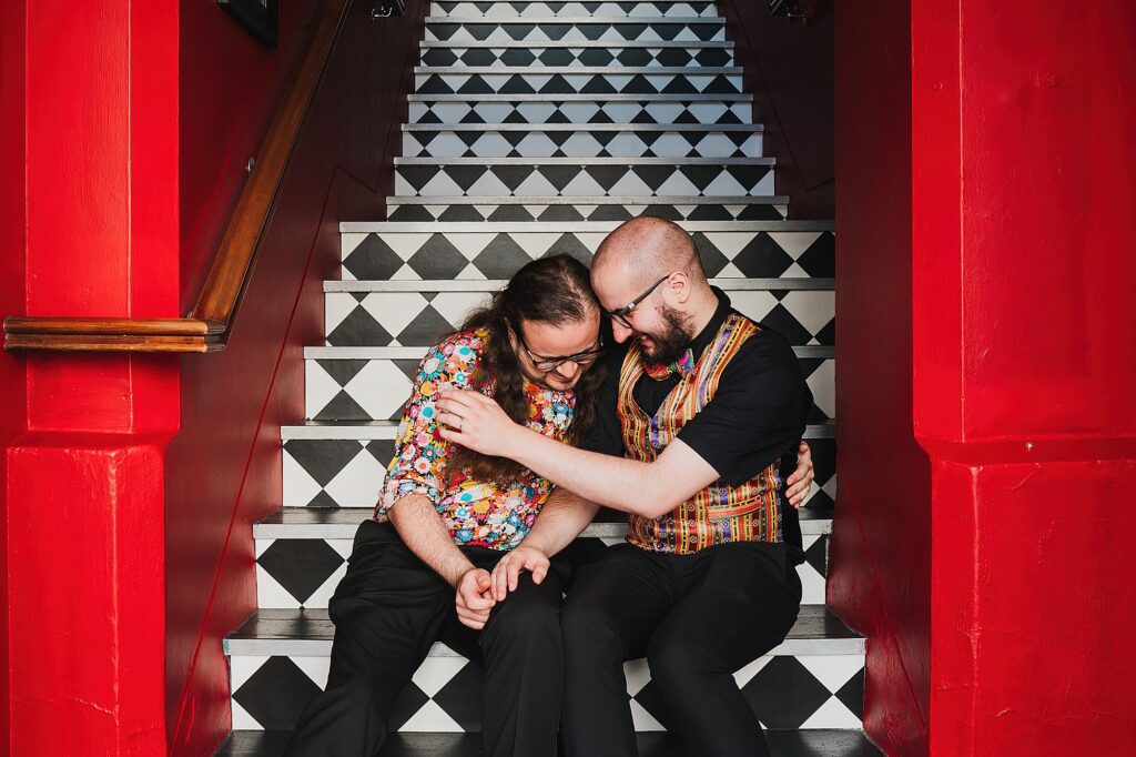 Gay couple giggling and laughing while say on the stairs at Oddfellows, Chester // Cheshire Wedding Photographer