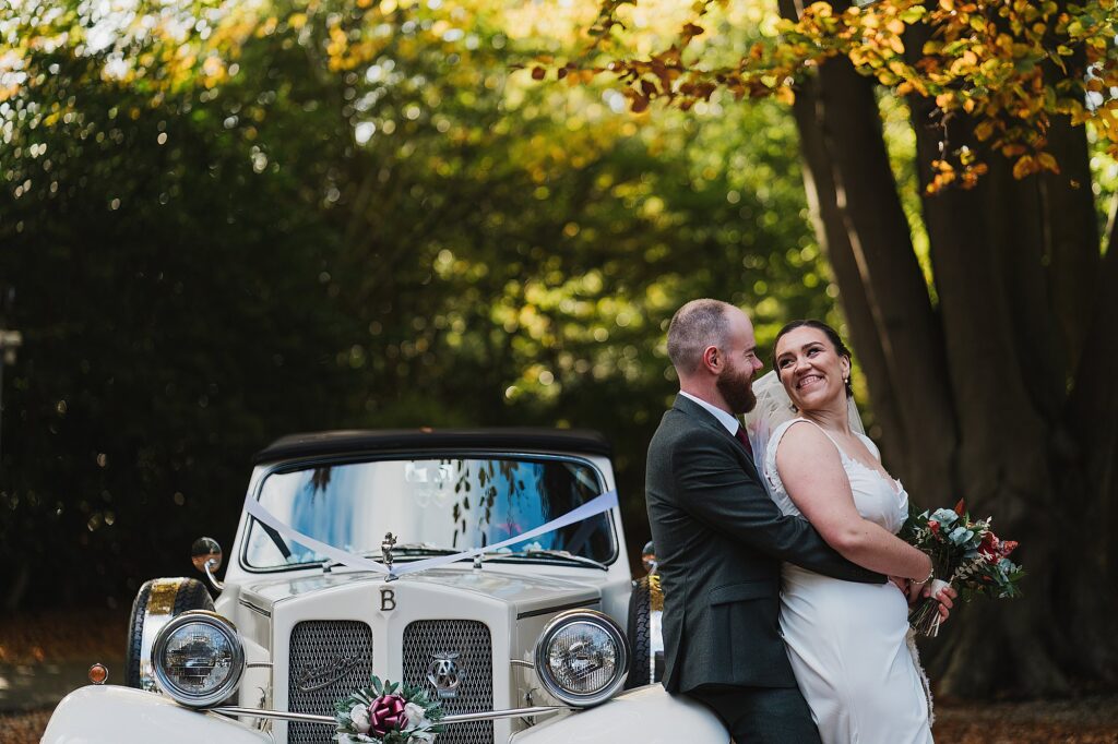 Bride and Groom portrait amongst the autumn leaves and with the wedding car
