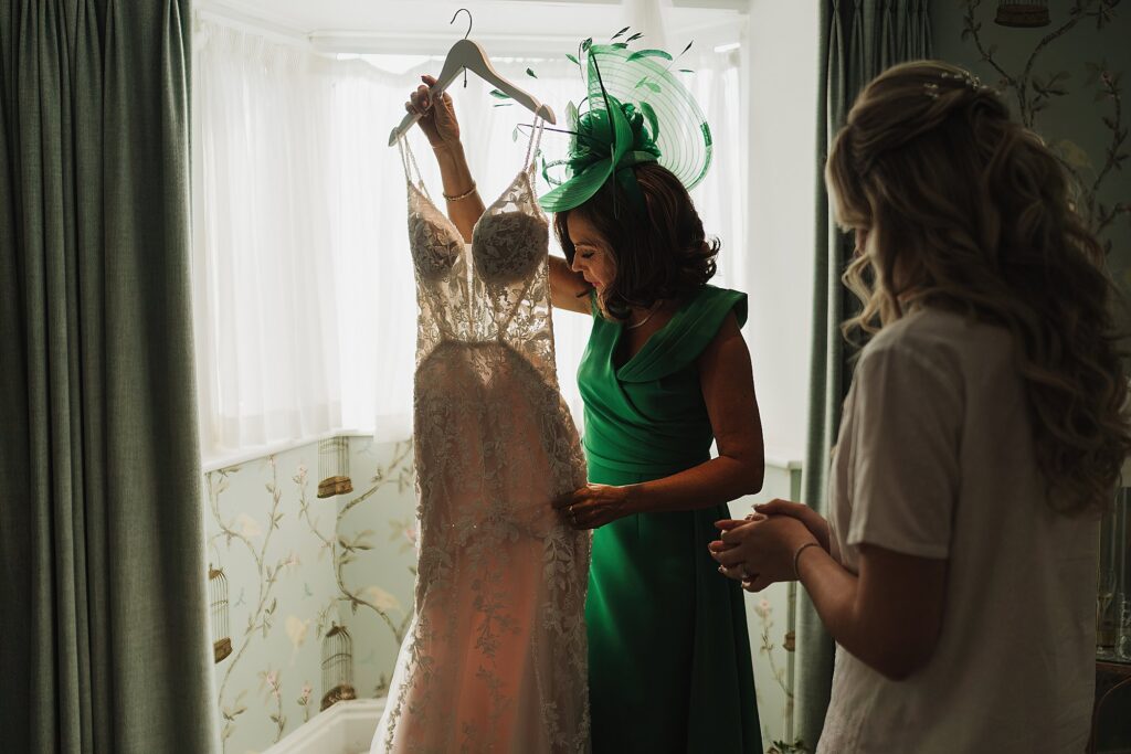 Mother of the bride getting the bride's dress ready for her in the Keeper's Cottage Combermere Abbey