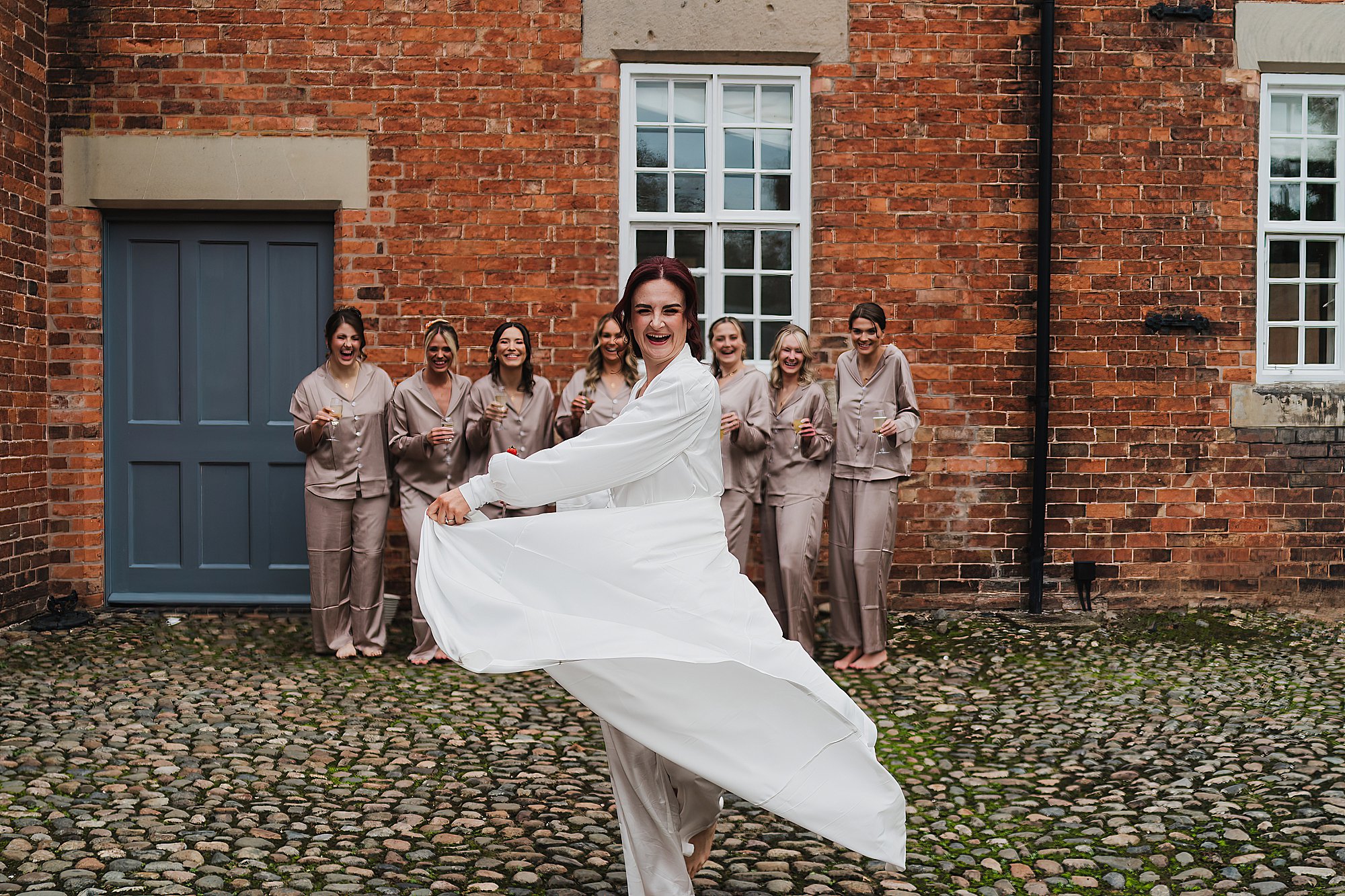 Bride messing around with her wedding gown with the bridesmaids outside the cottages at Combermere Abbey