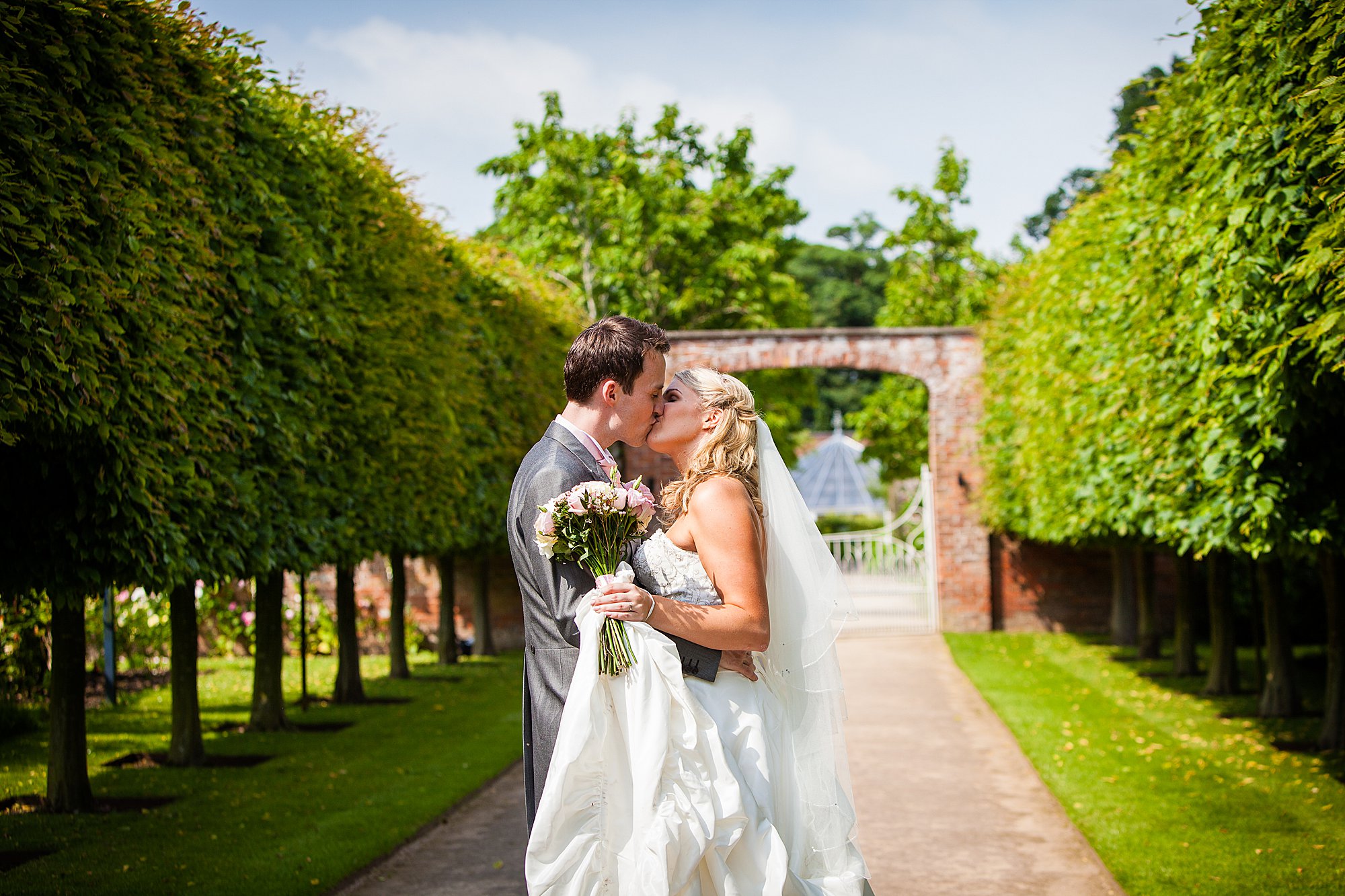 couple kissing in the tree lined walk way at combermere abbey